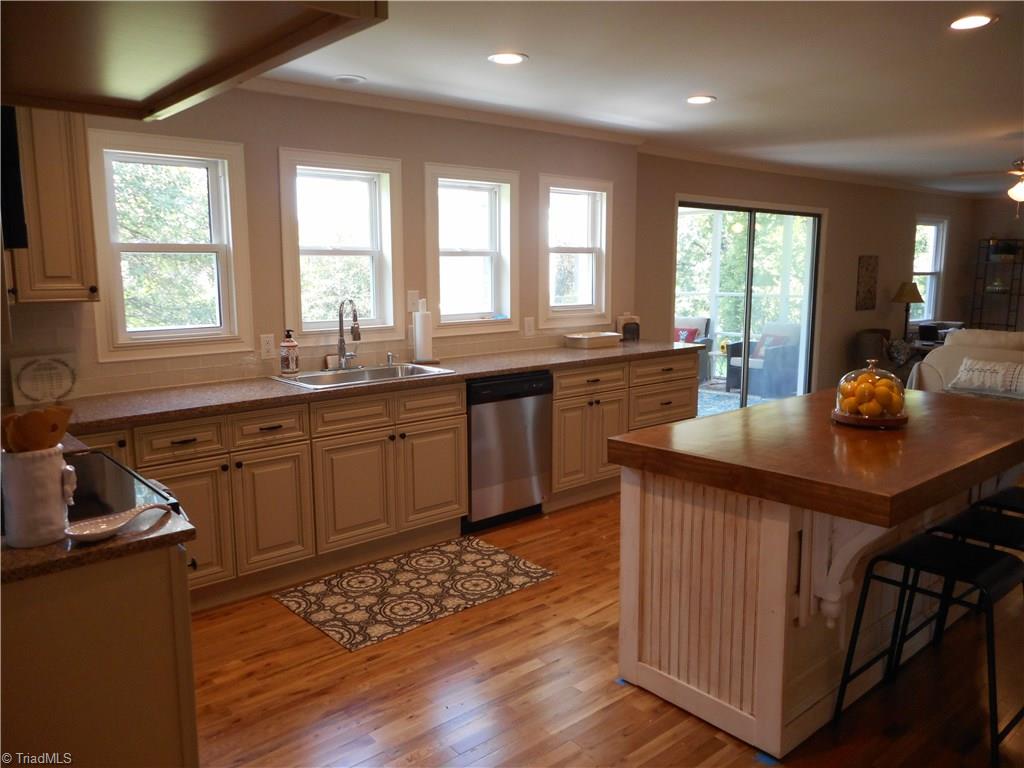 6346 Company Mill Road Climax, NC 27233 - Photo 20 of 30 In thi sview of the kitchen we have that four windows for natural lighting, the sliding door to the screened in porch, the kitchen island and the engineered wood flooring with the den to the far right side.