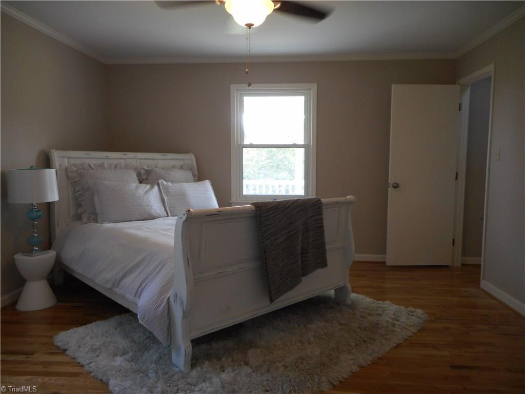 6346 Company Mill Road Climax, NC 27233 - Photo 21 of 30 In this view we are over by the master bathroom looking over the master bedroom. Here we can see one of the two windows for natural lighting, the engineered wood flooring, the ceiling fan with light and the open door to the right is to the dining room and front entry door.
