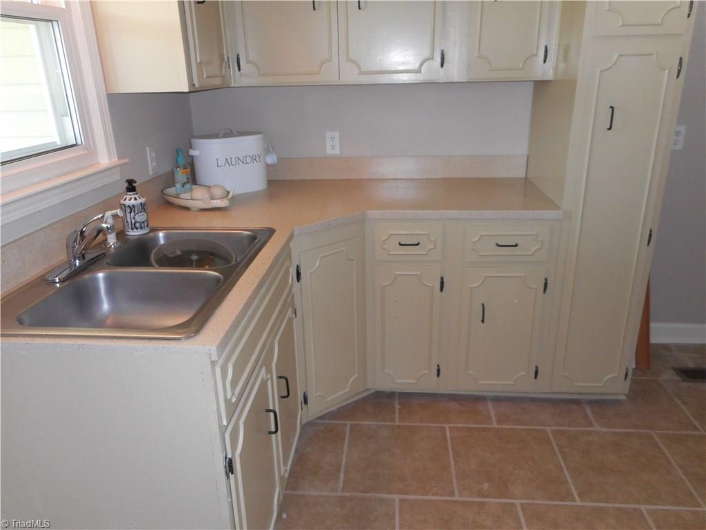 6346 Company Mill Road Climax, NC 27233 - Photo 29 of 30 In this view we are in the laundry room. Here we can see the window for natural lighting, the sink and cabinets and the tile flooring for easy cleaning. The washer and dryer hookups are behind us. Just to the right of the photo is the main level half bath and the entry door to the garage.