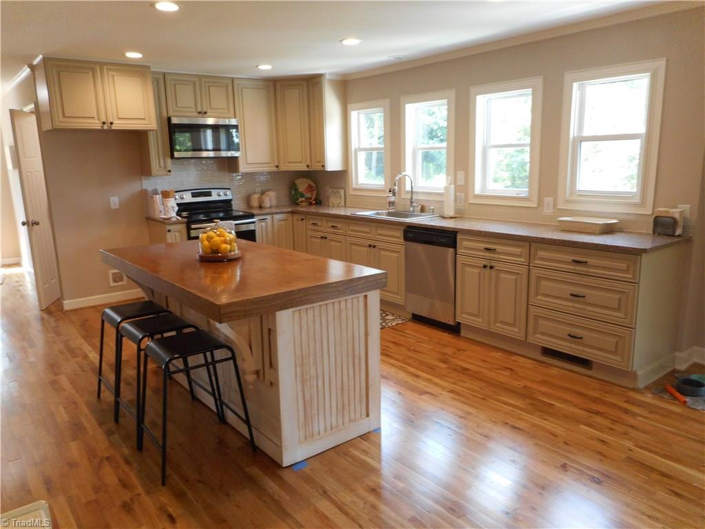 6346 Company Mill Road Climax, NC 27233 - Photo 4 of 30 In this view we are in the den looking into the kitchen. Here we have a nice view of the kitchen island, with stools you have a nice place for a casual dinner or lunch. You have the nice kitchen cabinets and the quartz counter tops, the tiled back splash for easy cleaning, recessed lighting, and look at all those windows for natural lighting. Another nice thing with having a window over the sink is that you can see what is going on in the backyard as you are cleaning up after a nice family dinner.