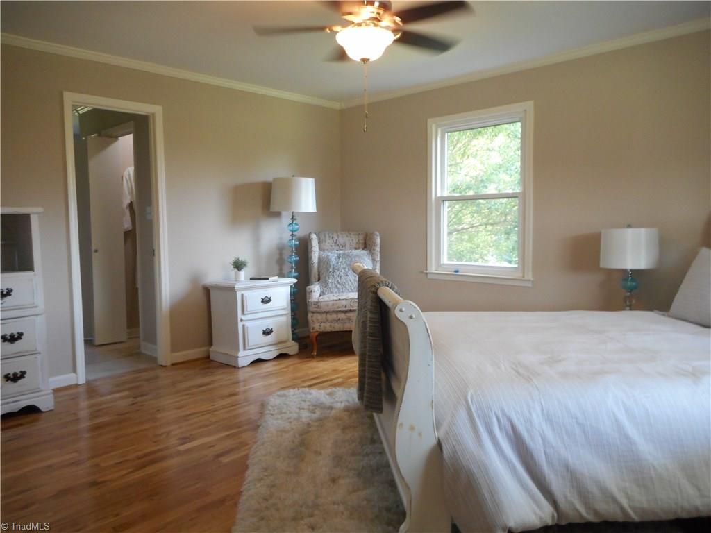 6346 Company Mill Road Climax, NC 27233 - Photo 5 of 30 In this view we are in the main level master bedroom. here we have engineered wood flooring, fresh new paint, crown molding, the ceiling fan with light and two windows for natural lighting. The open door is to the master bathroom area.