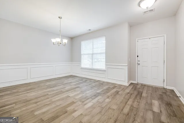 an empty room with wooden floor chandelier and windows