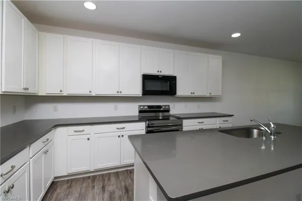 a kitchen with stainless steel appliances a sink dishwasher a stove top oven a refrigerator with white cabinets and a wooden floor