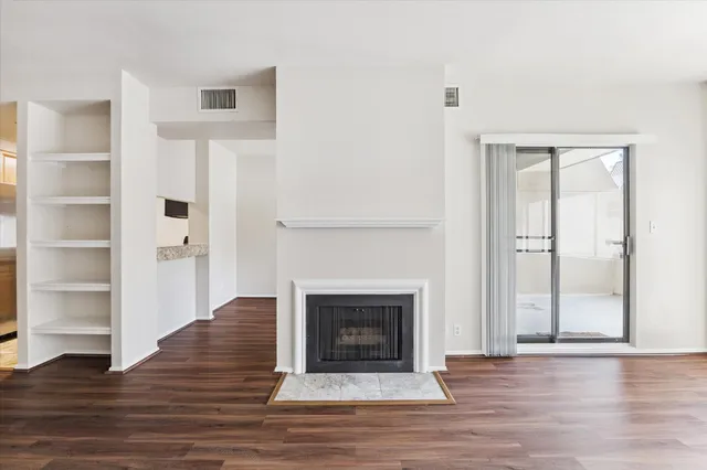 a view of an empty room with wooden floor fireplace and a window