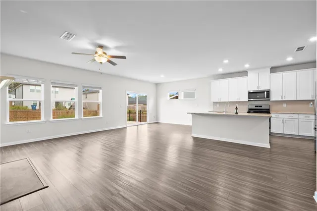 a view of an empty room with kitchen and window