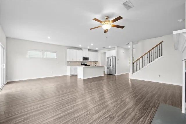 a view of an empty room with wooden floor and a ceiling fan