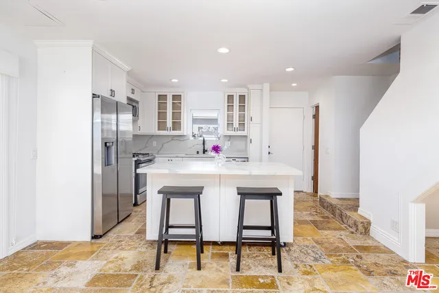 a kitchen with stainless steel appliances kitchen island granite countertop a kitchen island a stove a refrigerator and white cabinets with wooden floor