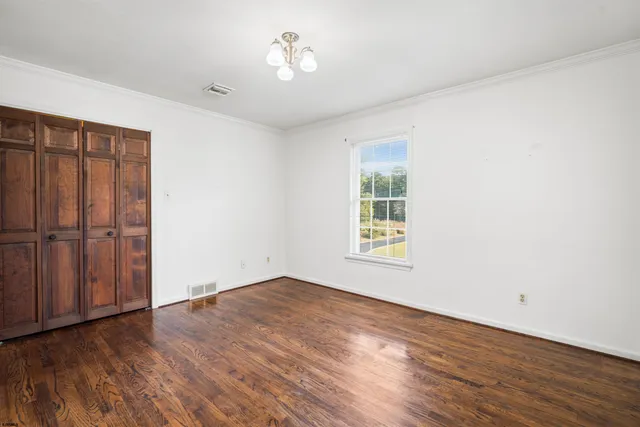 an empty room with wooden floor chandelier fan and windows