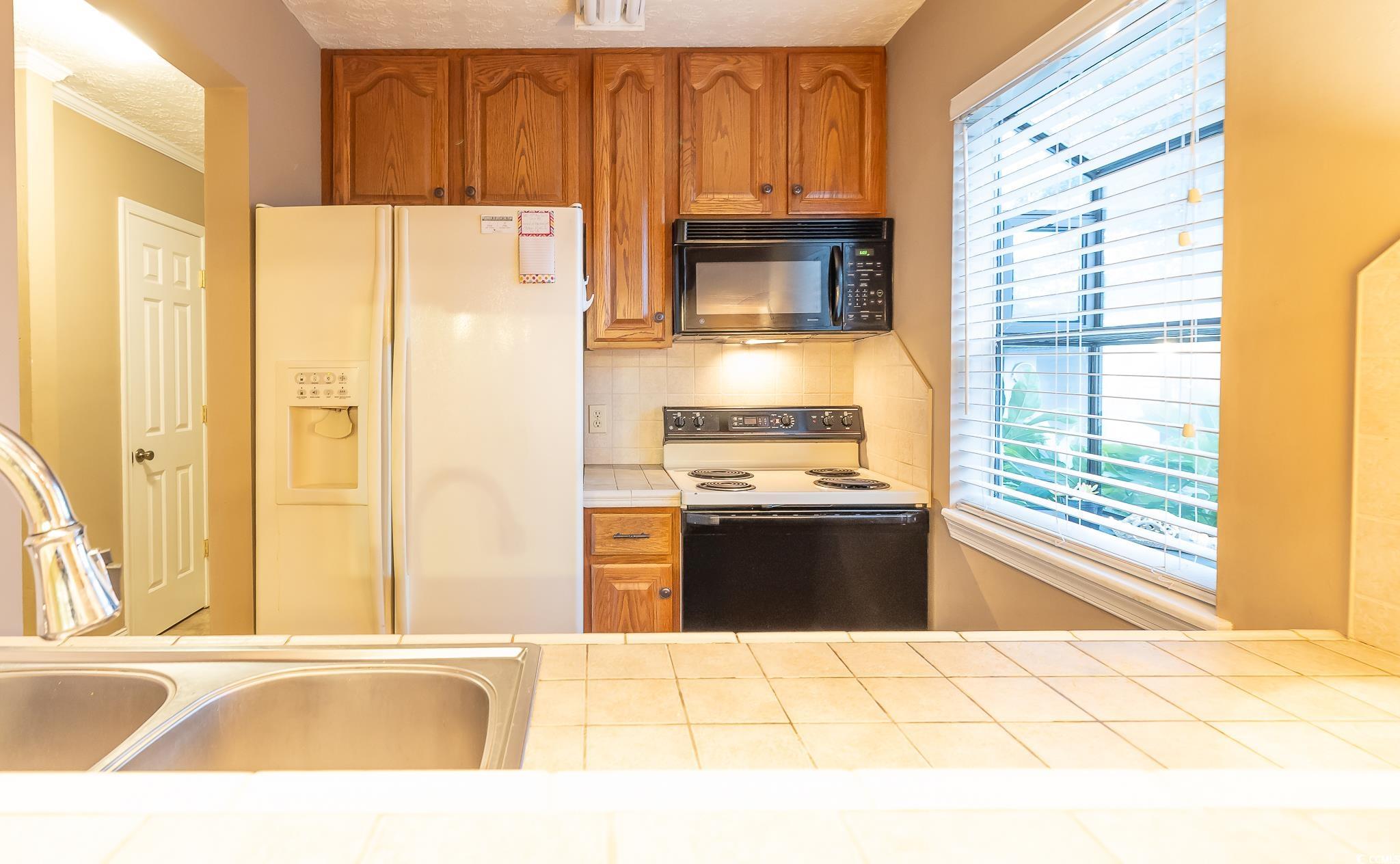 620 15th Avenue South, Unit 89 Surfside Beach, SC 29575 - Photo 4 of 14 Kitchen with white fridge with ice dispenser, range with electric stovetop, healthy amount of natural light, tile countertops, and crown molding