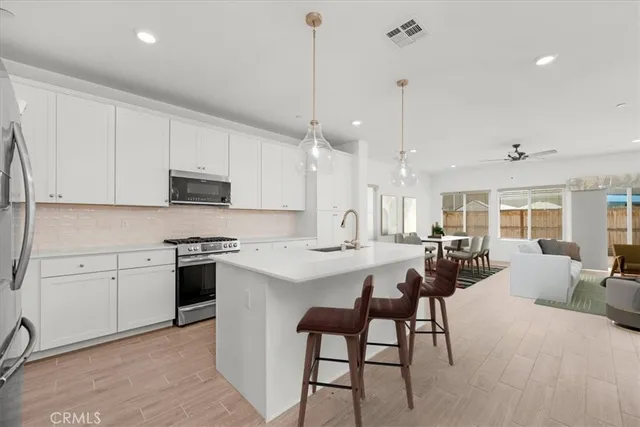 a large kitchen with kitchen island a stove a sink a refrigerator and white cabinets with wooden floor