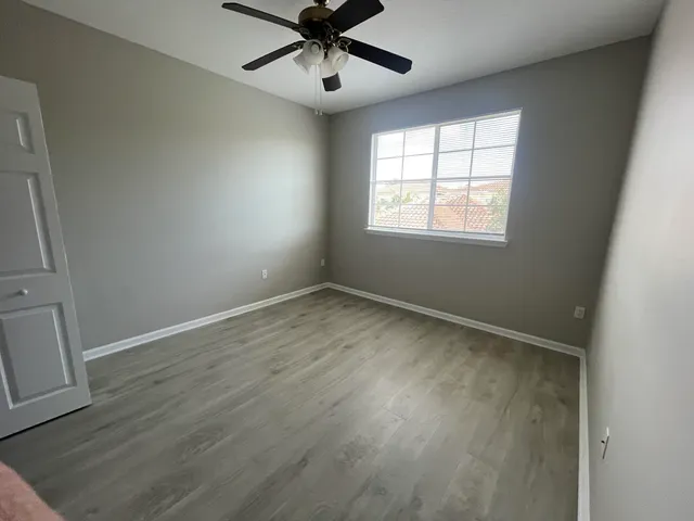 an empty room with wooden floor fan and windows