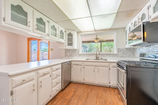 a kitchen with stainless steel appliances granite countertop a stove a sink dishwasher and white cabinets with wooden floor