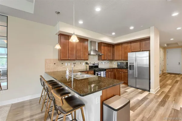 a kitchen with stainless steel appliances granite countertop a refrigerator a stove a sink a dining table and chairs with wooden floor