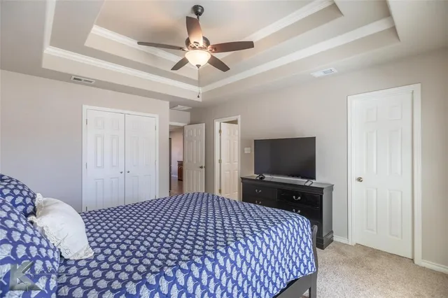 a spacious bedroom with a bed and a flat tv screen on dresser