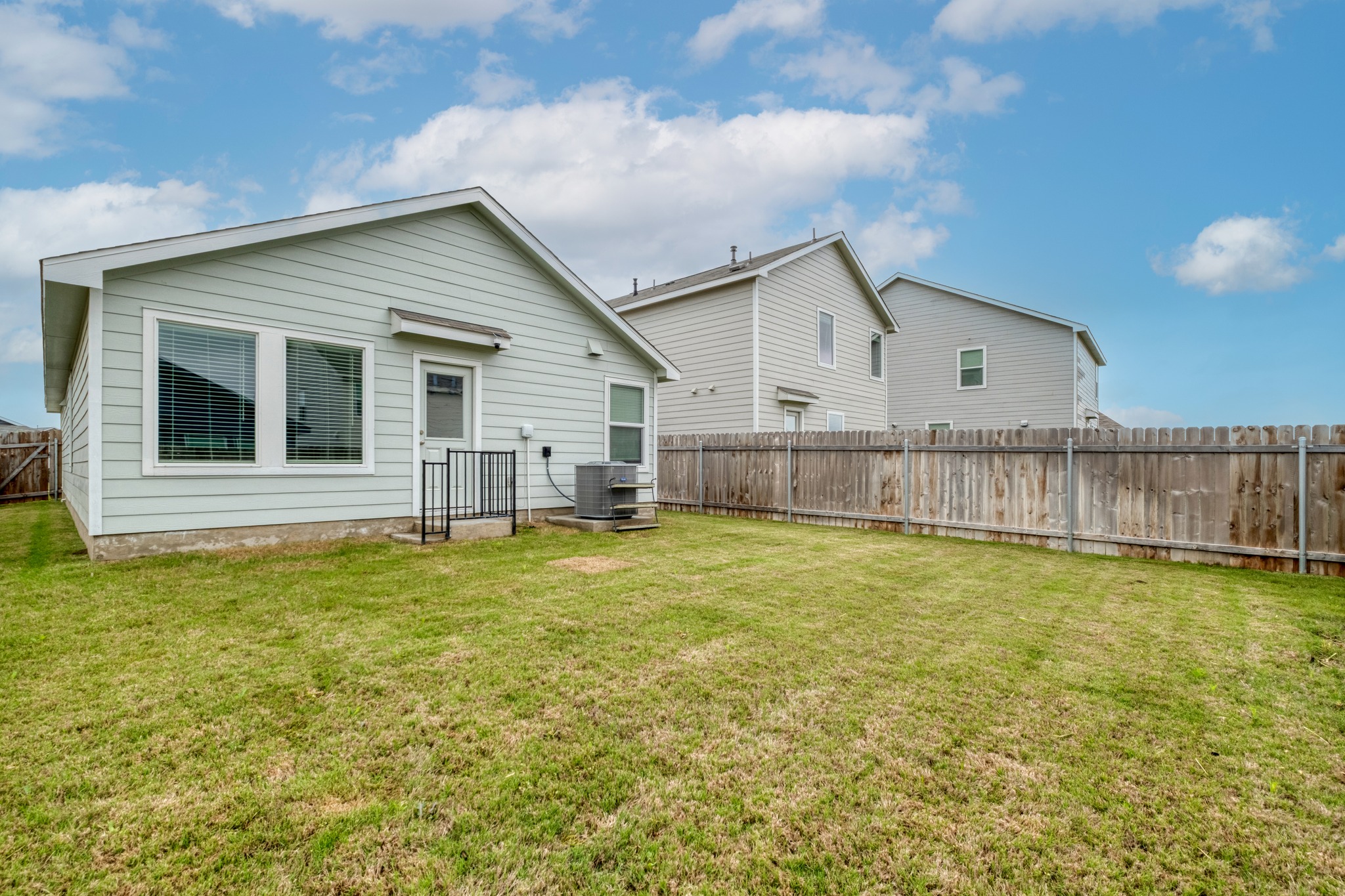 23412 Tiny Moons Way Elgin, TX 78621 - Photo 35 of 38 Expansive rear yard featuring green grass, a wood fence, and a light-colored siding exterior with multiple windows