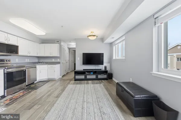 a living room with stainless steel appliances furniture a flat screen tv and a window