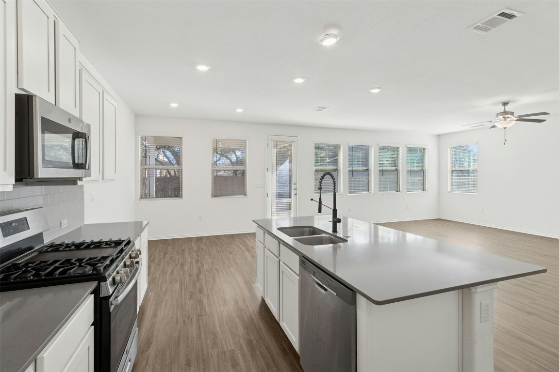 10405 Tree Duck Drive Austin, TX 78748 - Photo 31 of 33 Kitchen with appliances with stainless steel finishes, white cabinetry, open floor plan, dark wood finished floors, and decorative backsplash