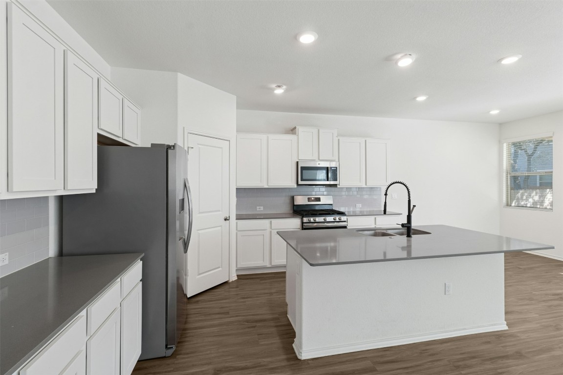 10405 Tree Duck Drive Austin, TX 78748 - Photo 9 of 33 Kitchen with appliances with stainless steel finishes, dark wood-style floors, backsplash, a center island with sink, and white cabinetry