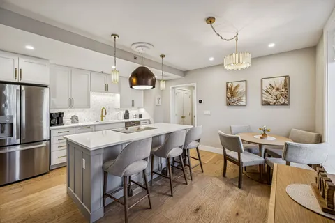 a kitchen with stainless steel appliances kitchen island granite countertop a dining table chairs and a refrigerator