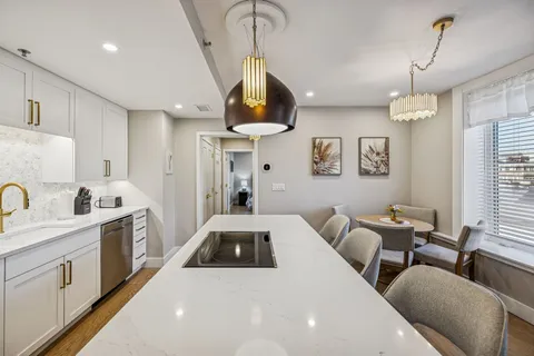 a kitchen with stainless steel appliances a stove a sink dishwasher a refrigerator white cabinets and couches with wooden floor