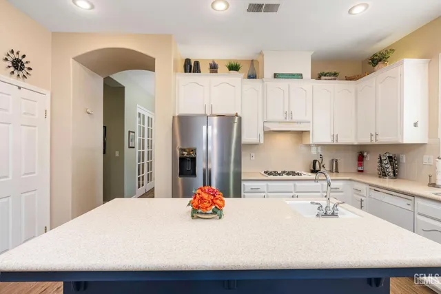 a kitchen with stainless steel appliances kitchen island granite countertop a refrigerator a sink dishwasher a stove with white cabinets and wooden floor