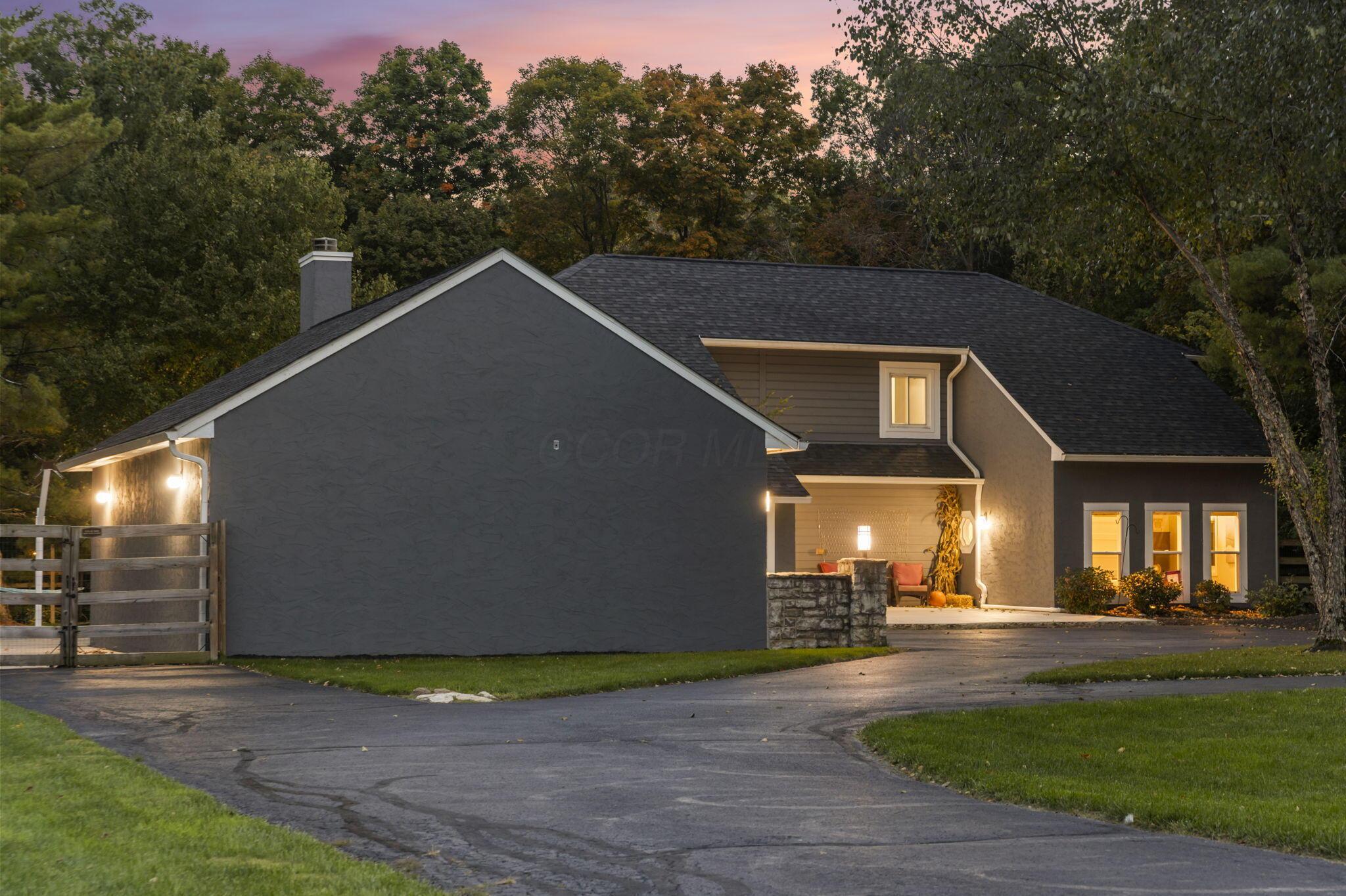 7140 Cook Road Powell, OH 43065 - Photo 19 of 87 Expansive paved driveway leading to a residence featuring a covered entry, stone column detailing, and a shingled roof