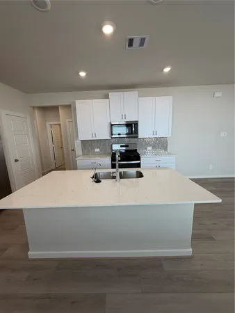 a large white kitchen with kitchen island a sink dishwasher a stove a refrigerator and cabinets with wooden floor