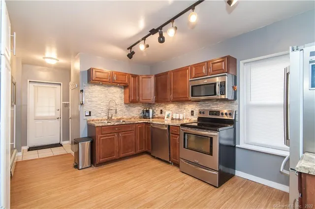 a kitchen with stainless steel appliances granite countertop a stove top oven a sink dishwasher a refrigerator and a microwave oven with wooden floor