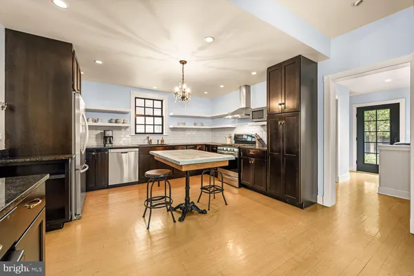 a kitchen with stainless steel appliances kitchen island granite countertop a refrigerator a stove a sink a dining table and chairs with wooden floor