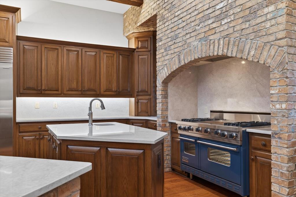 701 West Walcott Street Pilot Point, TX 76258 - Photo 12 of 40 Kitchen with high quality appliances, wood finished floors, an island with sink, light stone counters, and beamed ceiling
