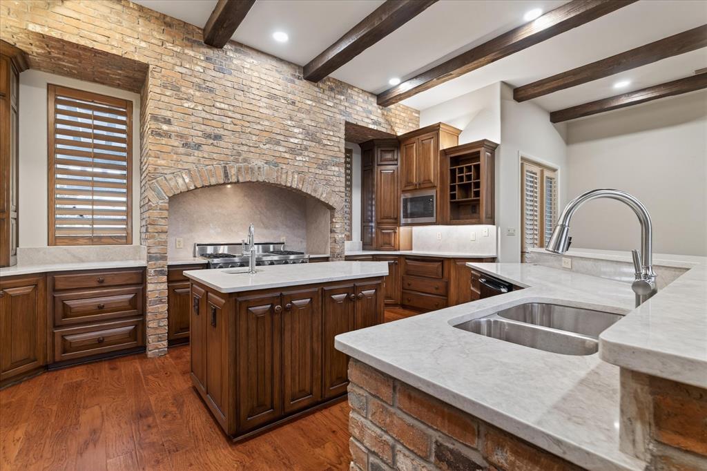 701 West Walcott Street Pilot Point, TX 76258 - Photo 14 of 40 Kitchen featuring an island with sink, dark wood-type flooring, light stone countertops, beamed ceiling, and stainless steel microwave