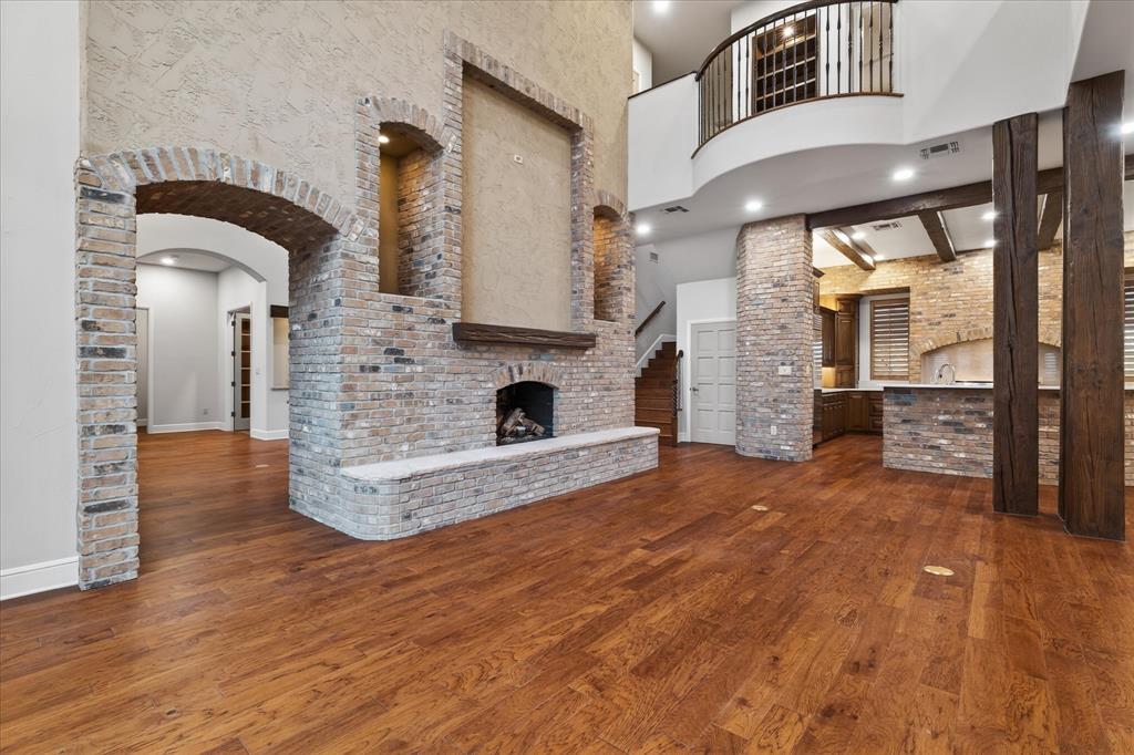 701 West Walcott Street Pilot Point, TX 76258 - Photo 18 of 40 Unfurnished living room with a high ceiling, a brick fireplace, brick wall, arched walkways, and dark wood-style floors