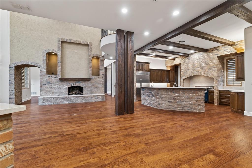 701 West Walcott Street Pilot Point, TX 76258 - Photo 22 of 40 Unfurnished living room with arched walkways, brick wall, a brick fireplace, dark wood finished floors, and beam ceiling