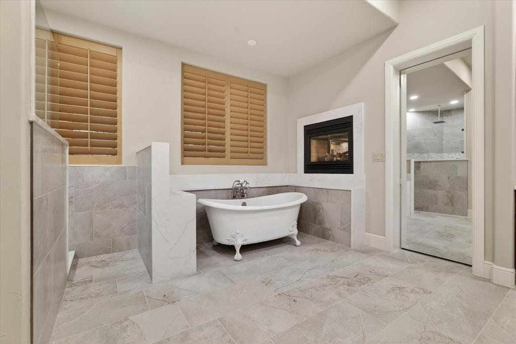 701 West Walcott Street Pilot Point, TX 76258 - Photo 26 of 40 Full bathroom featuring tile walls, walk in shower, a soaking tub, a glass covered fireplace, and wainscoting