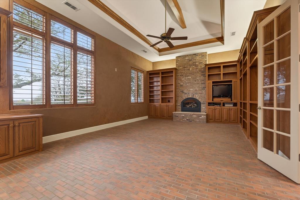 701 West Walcott Street Pilot Point, TX 76258 - Photo 32 of 40 Unfurnished living room with a ceiling fan, brick flooring, a brick fireplace, a raised ceiling, and built in features