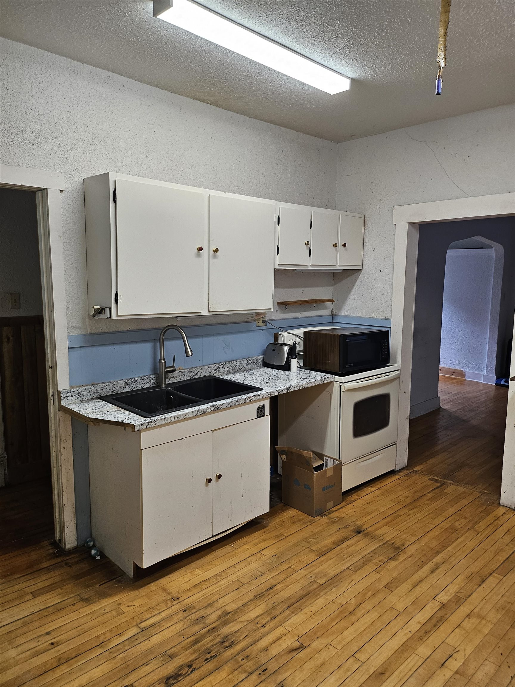 917 East 7th Street Duluth, MN 55805 - Photo 16 of 17 Kitchen featuring white cabinetry, a textured wall, light wood-style flooring, arched walkways, and a textured ceiling