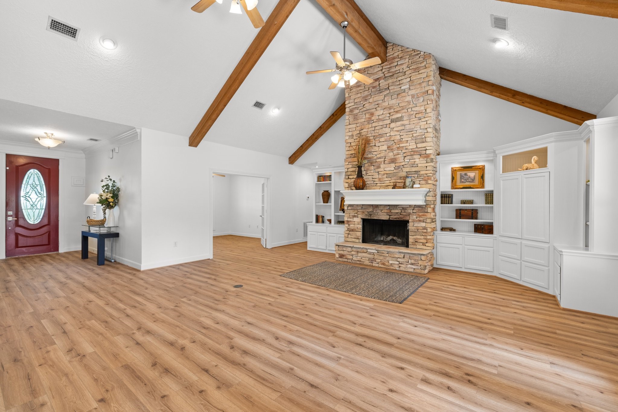 34310 High Point Drive Magnolia, TX 77355 - Photo 9 of 48 This spacious living room features a high vaulted ceiling with exposed wood beams, a beautiful floor to ceiling stone fireplace, and built-in shelving. The open layout and natural light create a warm, inviting atmosphere, complemented by vinyl plank flooring and a stylish entry door.