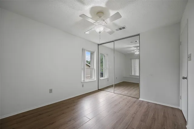 an empty room with wooden floor fan and windows