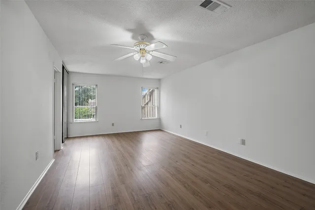 an empty room with wooden floor fan and windows