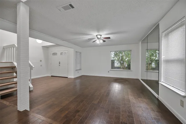 an empty room with wooden floor chandelier fan and windows