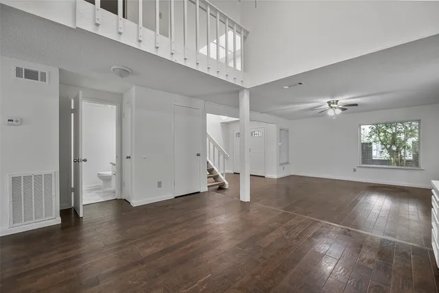 an empty room with wooden floor chandelier fan and windows