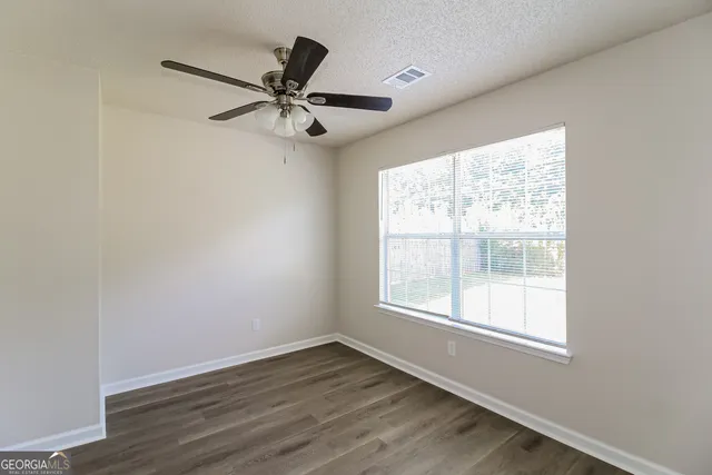an empty room with wooden floor fan and windows