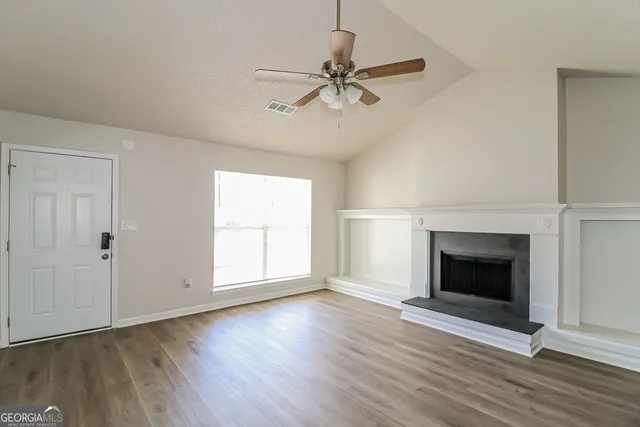 an empty room with wooden floor fireplace and windows