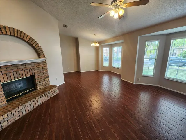 a view of an empty room with wooden floor fireplace and a window