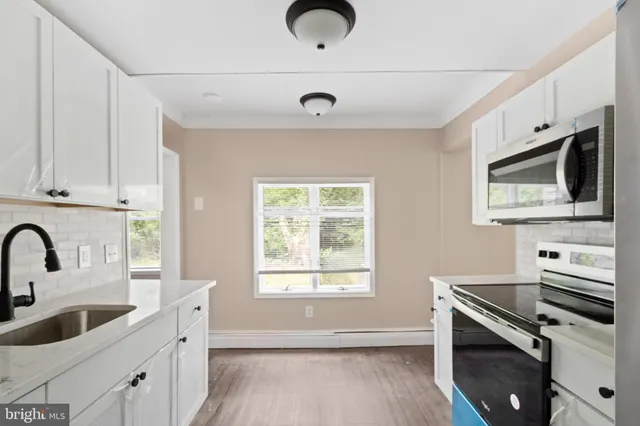 a kitchen with stainless steel appliances granite countertop a sink a stove a microwave a window and white cabinets