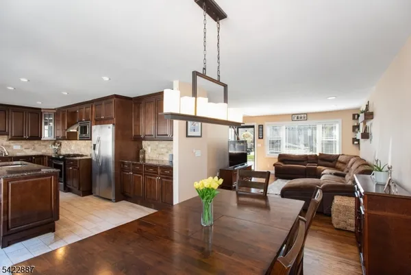 a kitchen with stainless steel appliances kitchen island granite countertop a refrigerator a stove a sink a dining table and chairs with wooden floor