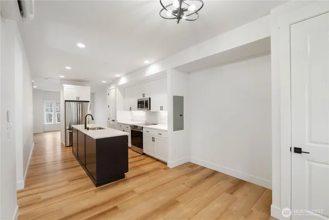 a living room with stainless steel appliances kitchen island hardwood floor and a sink