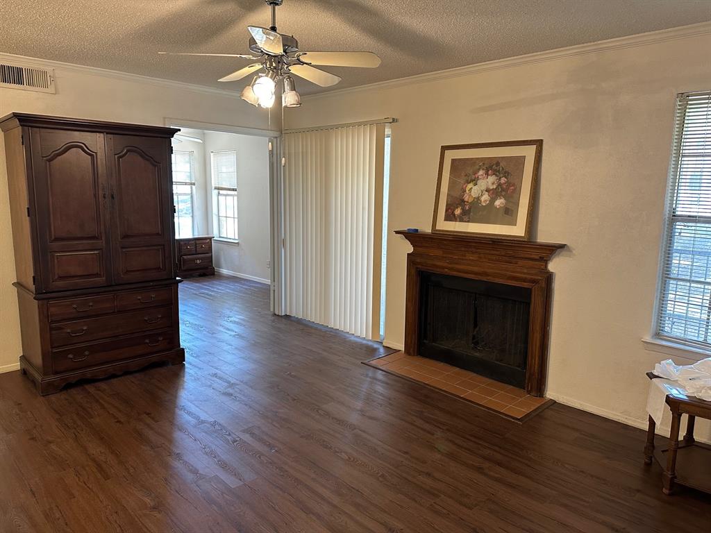 Unfurnished living room featuring plenty of natural light, a ceiling fan, dark wood finished floors, crown molding, and a textured ceiling