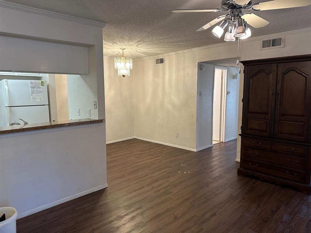 5300 Keller Springs Road, Unit 1090 Dallas, TX 75248 - Photo 7 of 10 Empty room with ceiling fan, dark wood finished floors, ornamental molding, a textured ceiling, and a chandelier