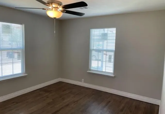 an empty room with wooden floor chandelier fan and windows